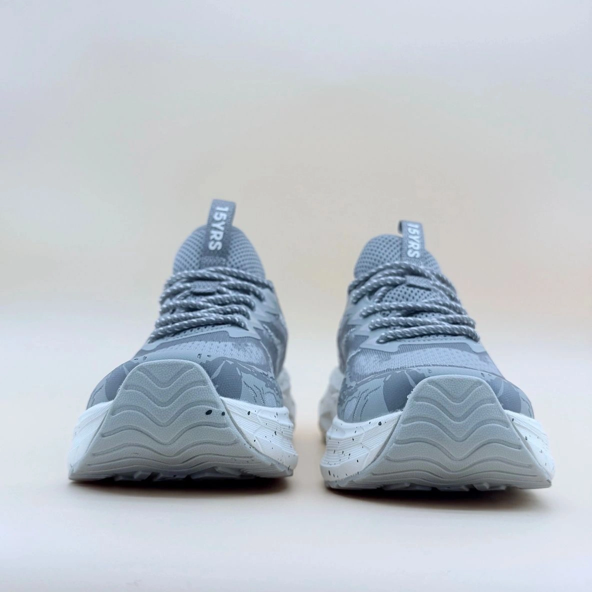 Gray sneakers with white soles, front view.